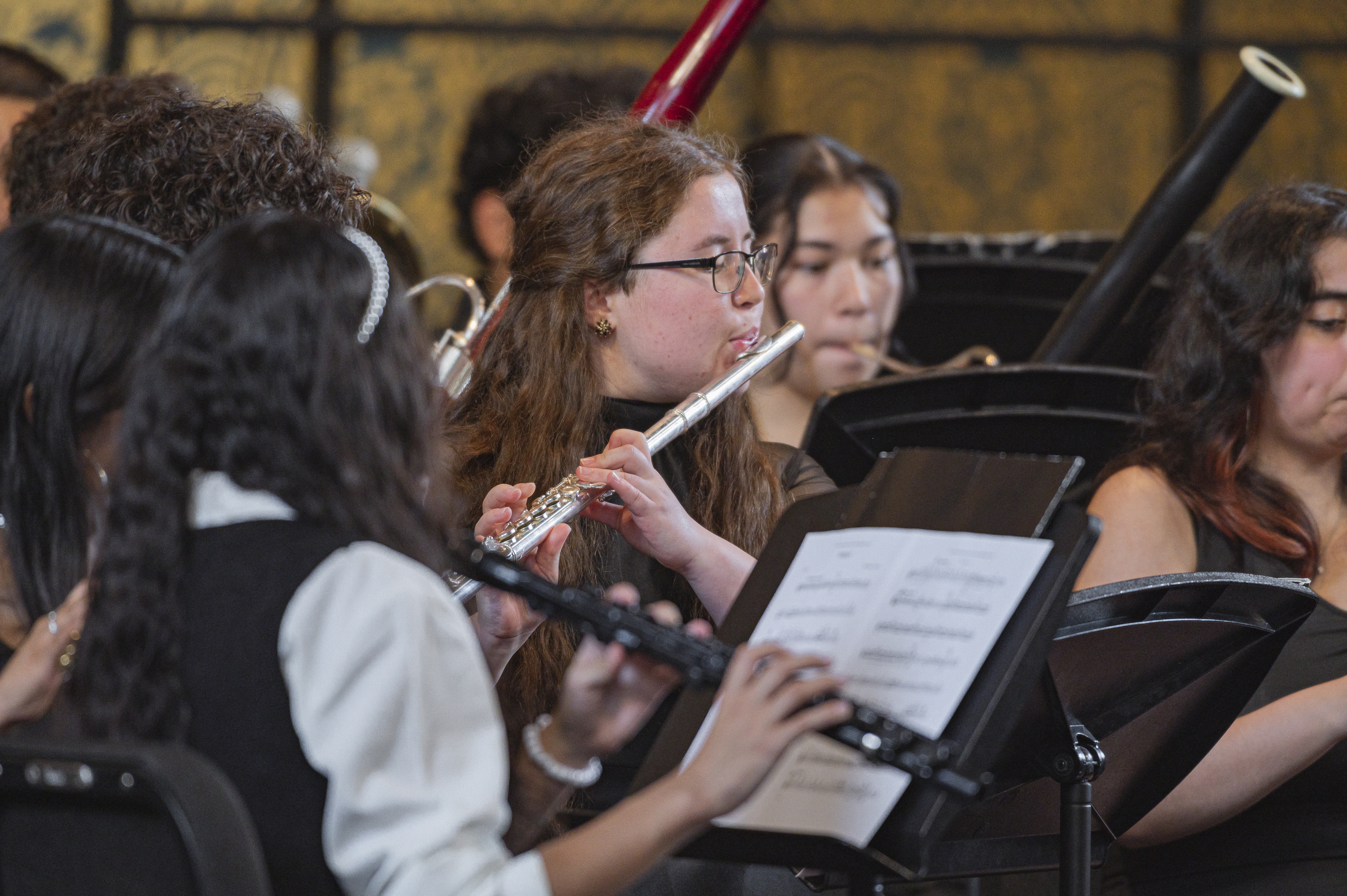 Girl with red-brown hair playing the flute surrounded by orchestra